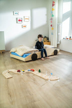 Bolide autobed in naturel hout in een lichte kinderkamer, kind op het bed