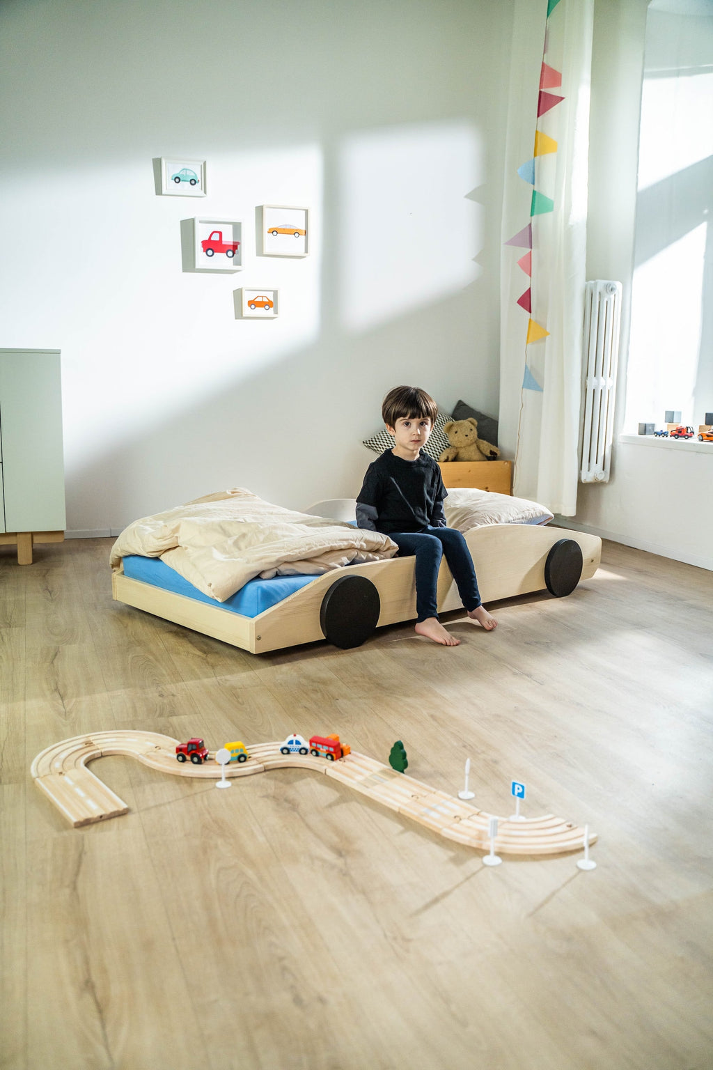 Bolide autobed in naturel hout, kind zit op het opgemaakte bed