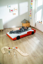 Racer autobed 80×160 in rood met slapend kind en houten autobaan ernaast