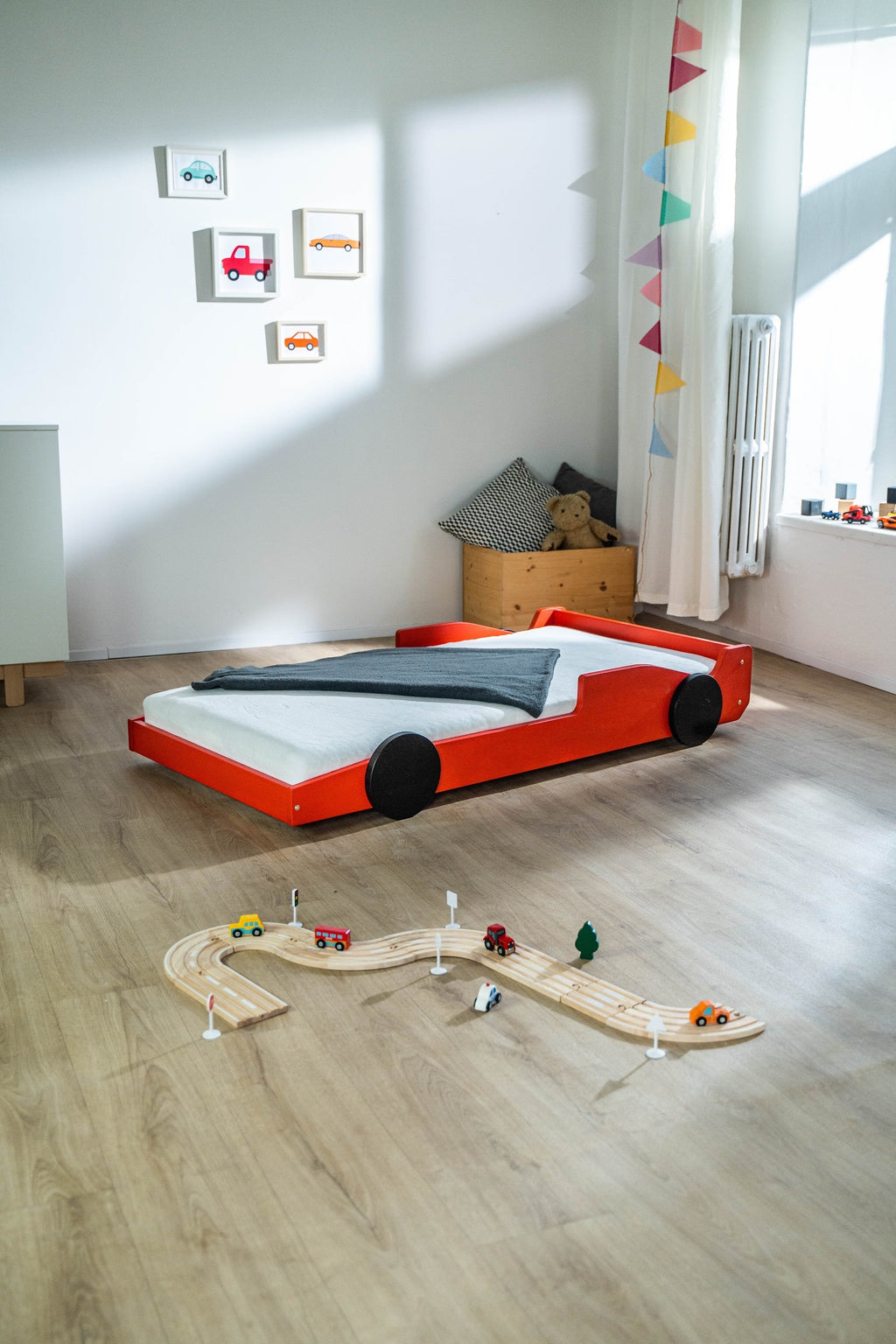 Racer autobed 80×160 in rood, schuin achteraanzicht in een kinderkamer met houten autobaan