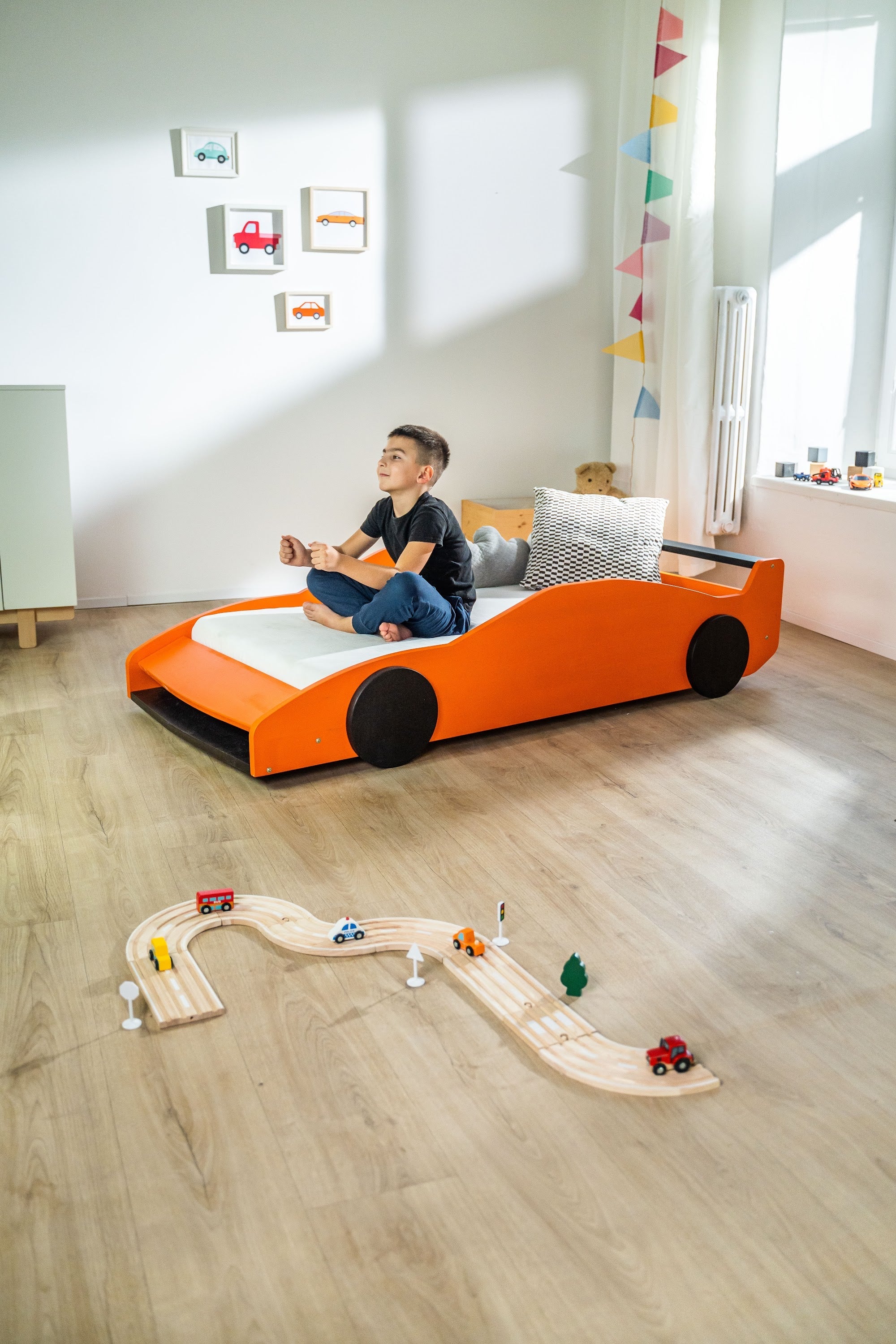 Turbo GT autobed 80×160 in oranje, kind zit op het bed in een lichte kinderkamer