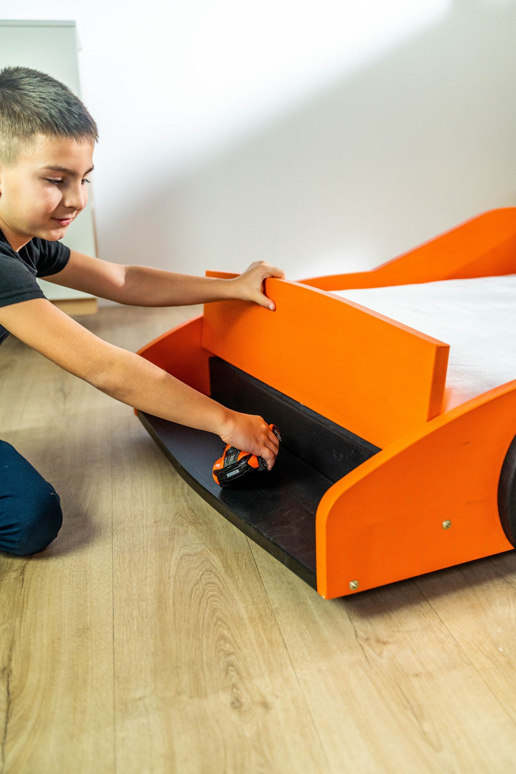 Turbo GT autobed 80×160 in oranje, kind pakt een speelgoedauto uit het opbergvak onder de neus